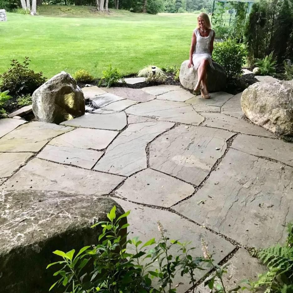Person sitting on a stone patio beside a green lawn and large rocks