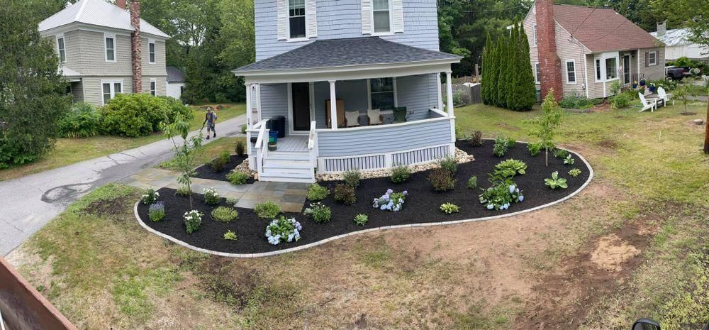 White two-story house with a front porch and newly landscaped flower bed, seen from the street.