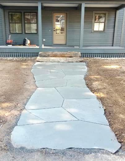 Concrete walkway leading to a blue house porch with a front door and windows