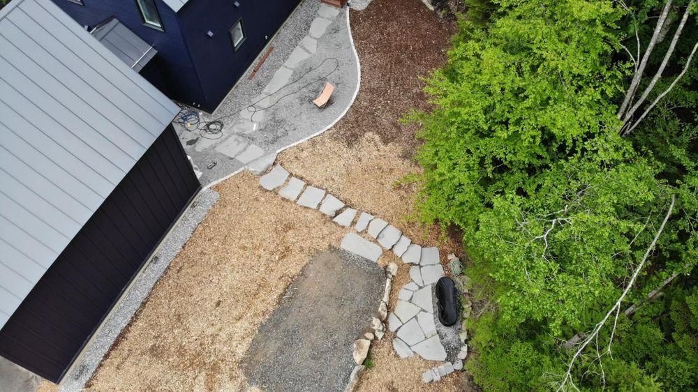 Aerial view of a gravel path beside a house, with stone edging and a green wooded area.