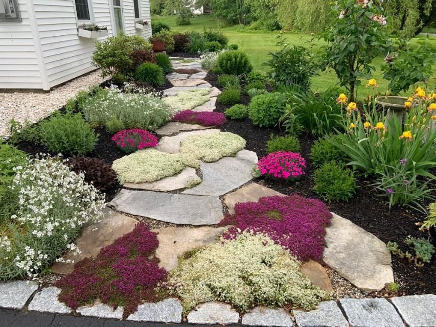 Curved stone garden path bordered by pink, white, and purple flowers beside a house