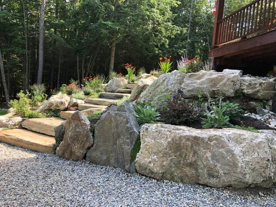Stone garden path beside large boulders and a wooden deck in a wooded landscape