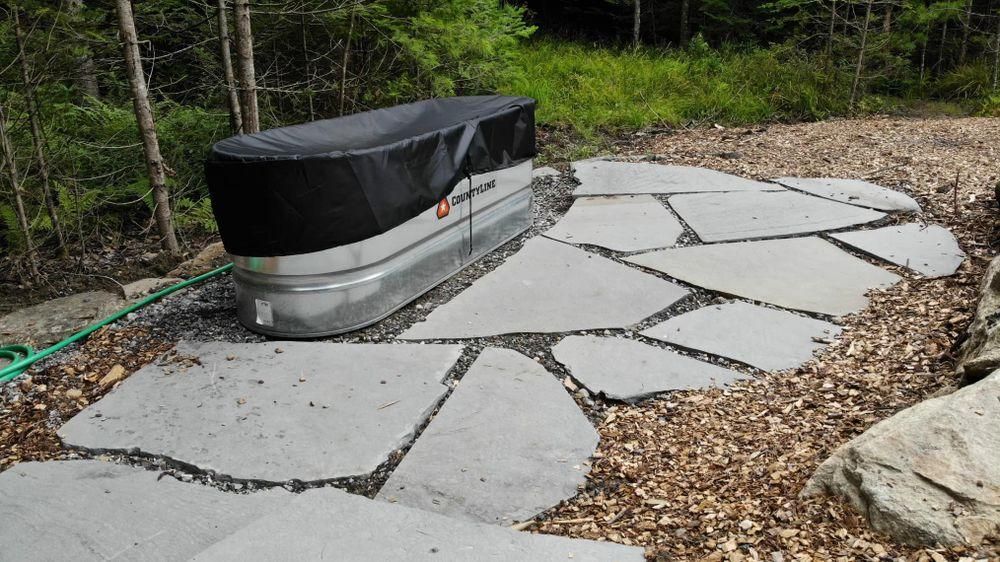 Concrete patio with irregular slab pavers around a covered hot tub in a wooded yard