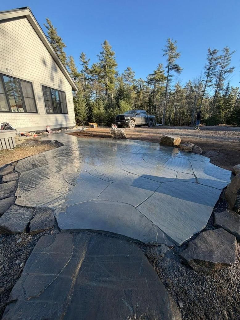 Icy backyard patio beside a house, with snow, rocks, and trees in bright sunlight