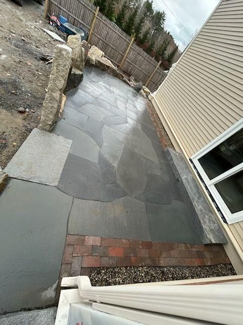 Sloped backyard patio with gray pavers, brick steps, gravel edge, and beige house siding