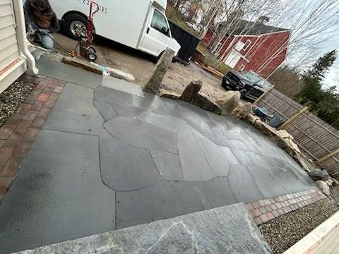 Gray flagstone patio under construction beside a driveway, with stone edging and a white truck nearby