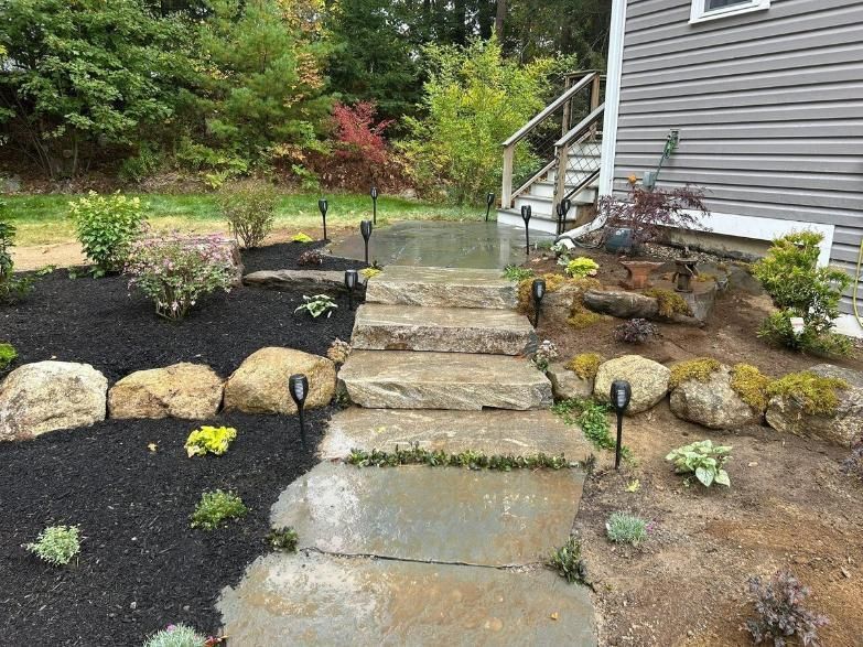 Stepping-stone path leading to a house entrance through a landscaped garden with rocks and shrubs