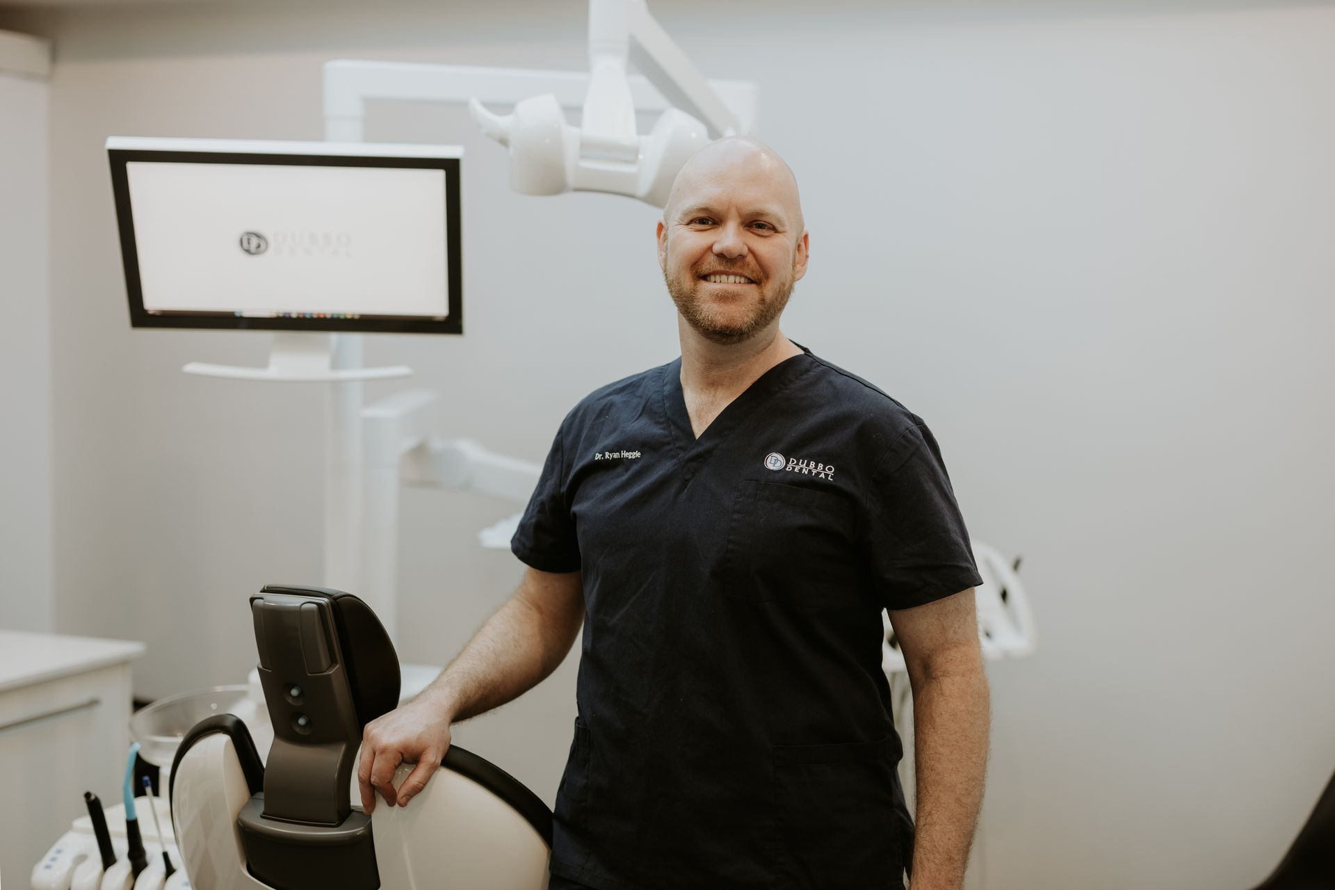 Dentist in a Dark Blue Scrub Smiling in an Exam Room With Equipments — Dubbo Dental in Dubbo, NSW