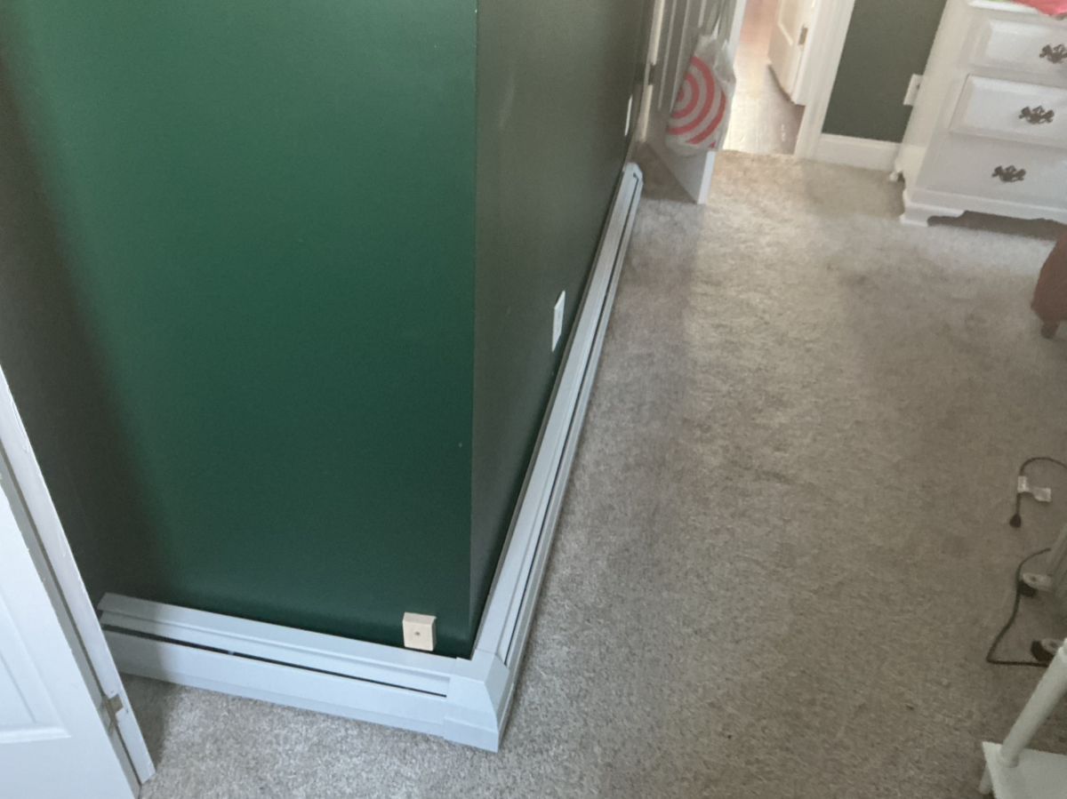 A white baseboard heater runs along a dark green wall in a carpeted room.