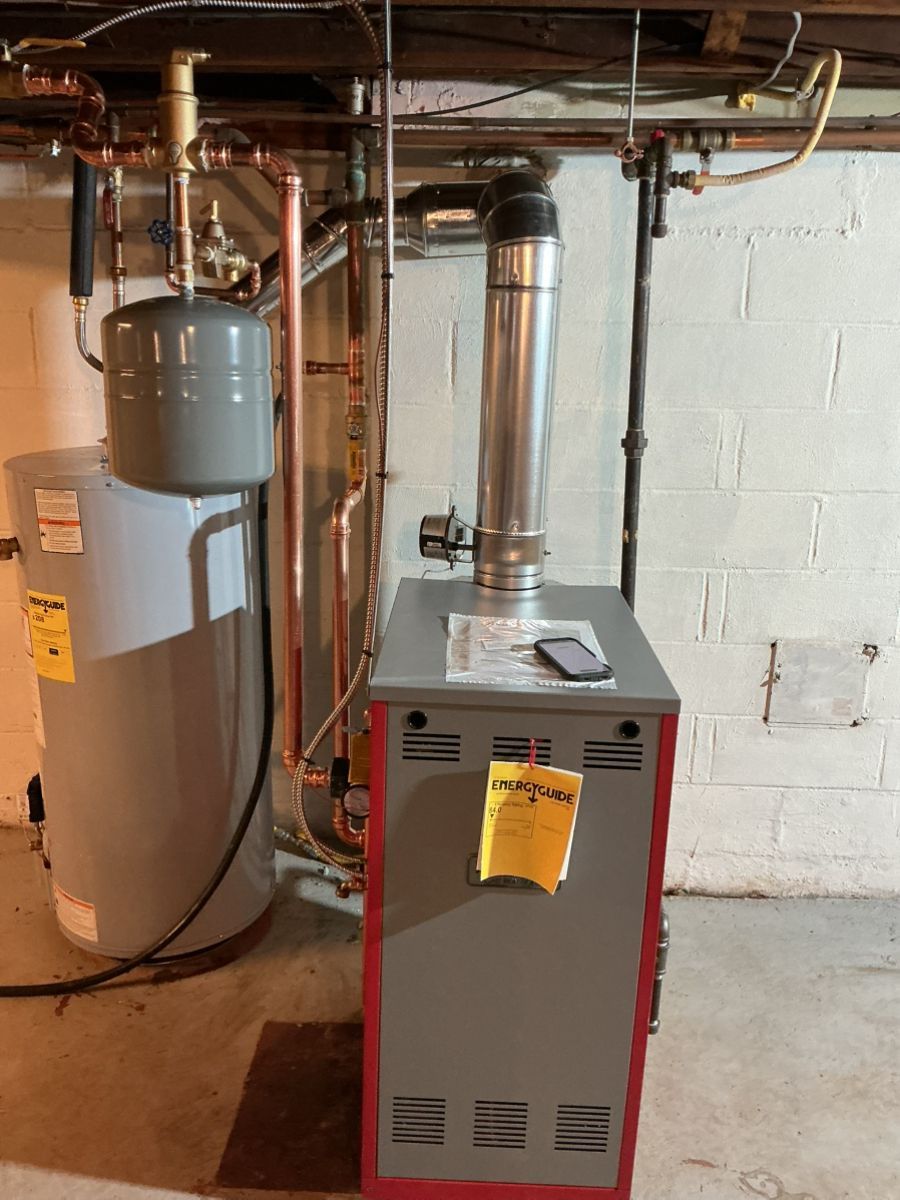 A basement utility area featuring a water heater with an expansion tank next to a red furnace with a silver flue pipe.