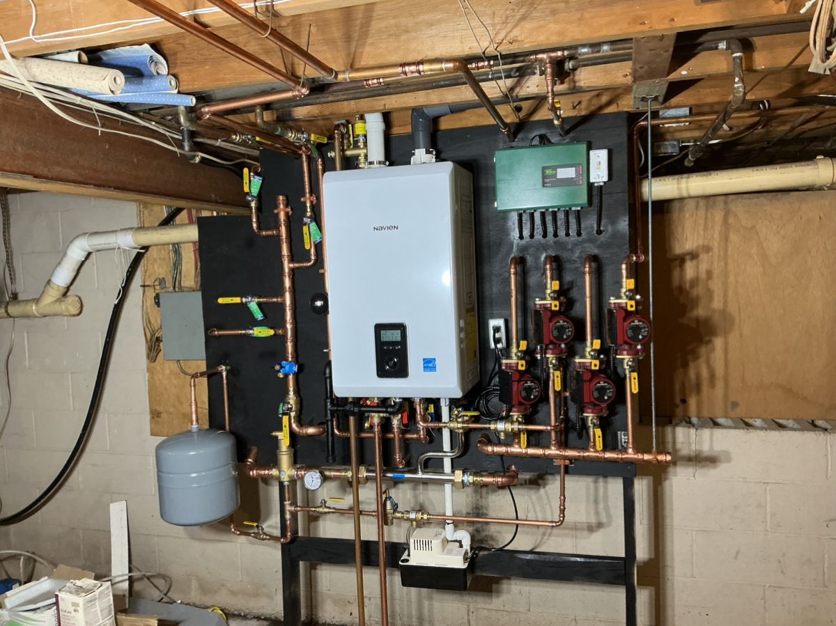 A wall-mounted high-efficiency boiler and plumbing system with multiple red pumps and a grey expansion tank in a basement.