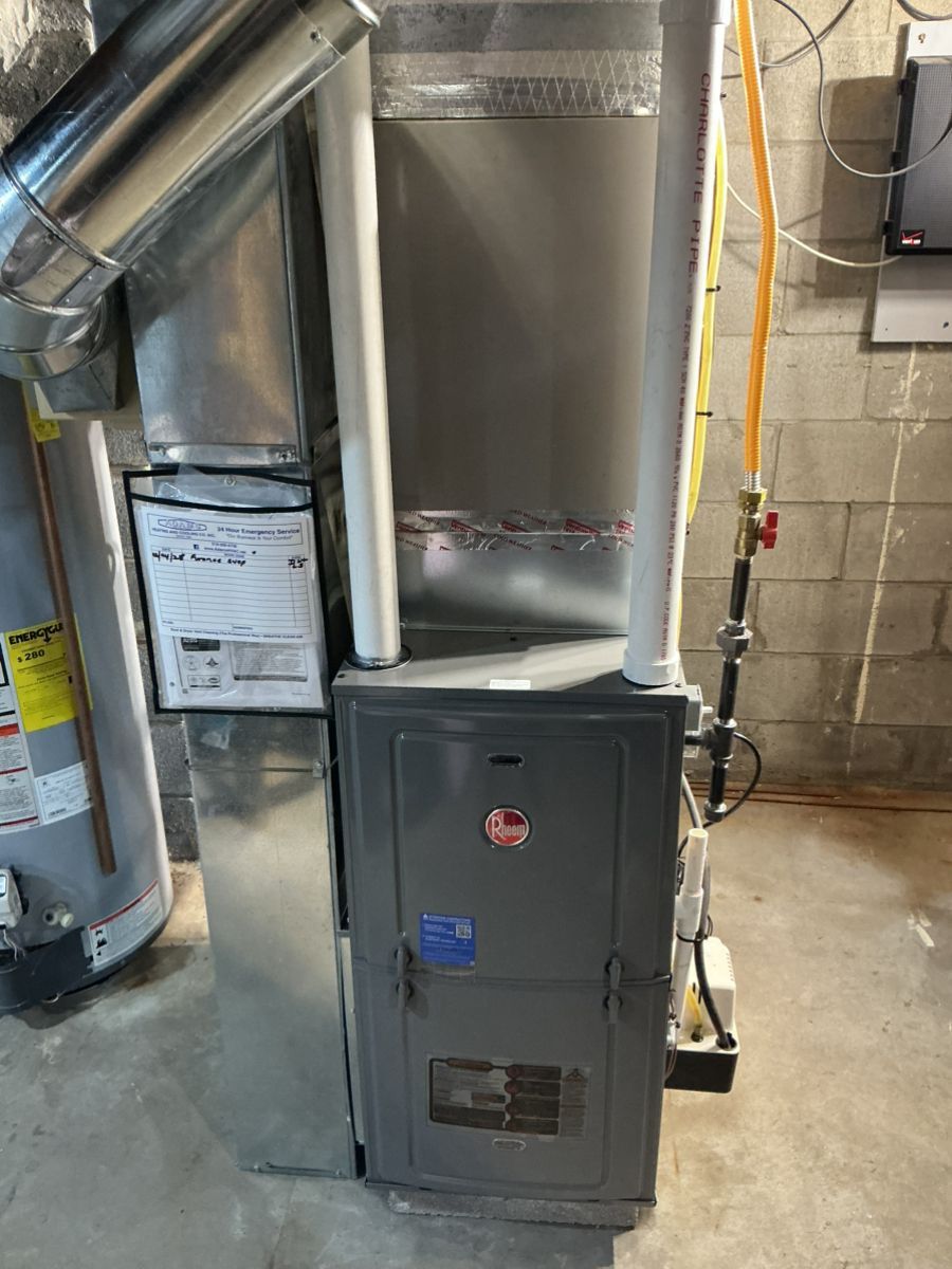 A grey Rheem furnace with white intake and exhaust pipes in a basement next to a water heater.