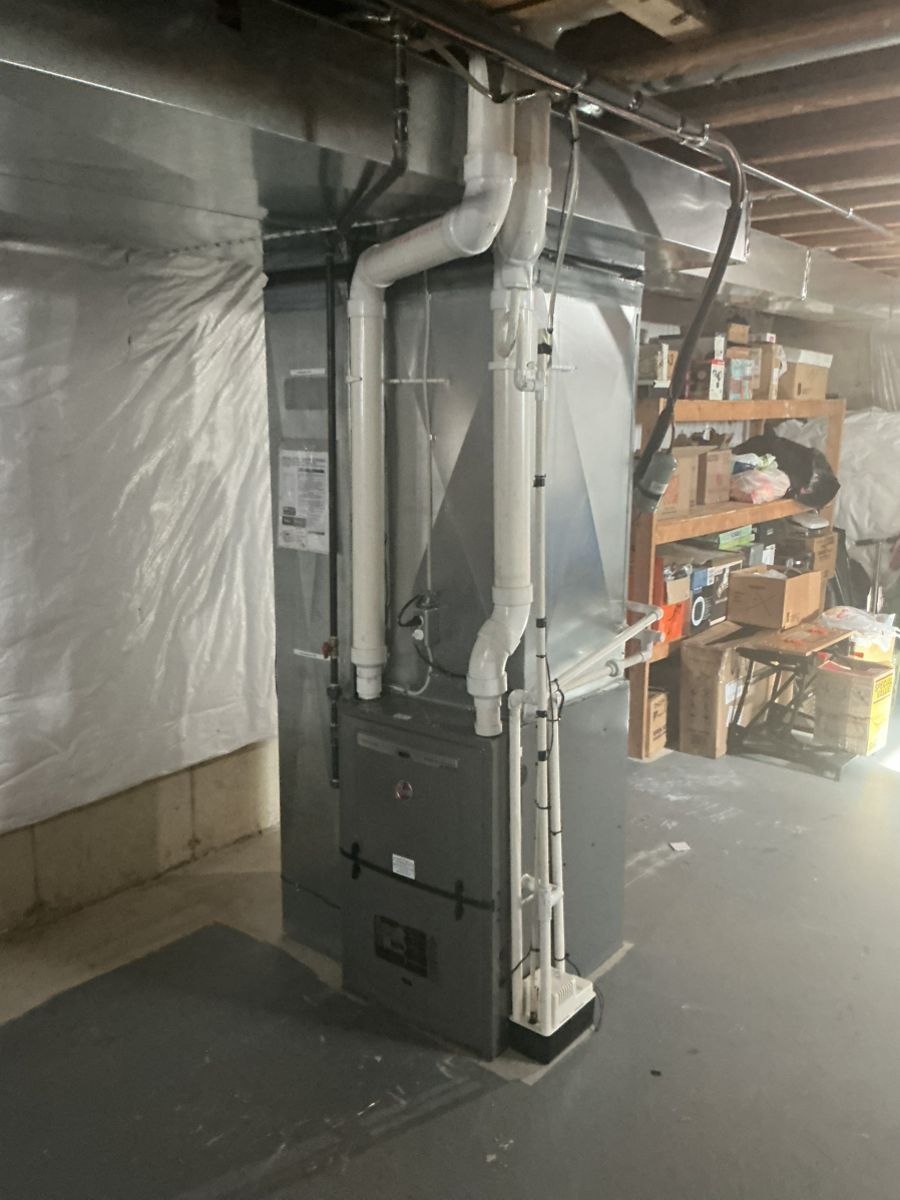 A silver high-efficiency furnace stands in a basement with white PVC exhaust pipes attached to its top and side.