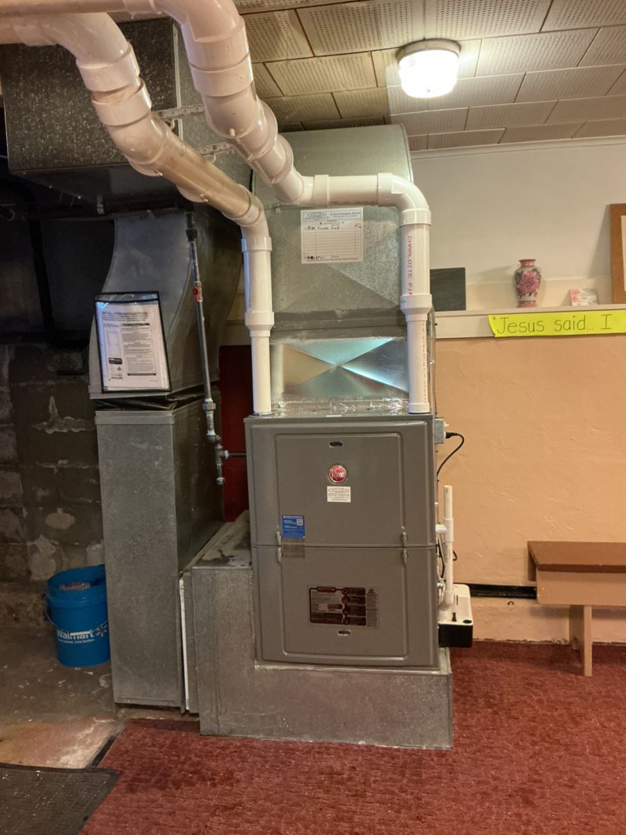 A furnace unit with white PVC vent pipes installed on a concrete base in a basement.