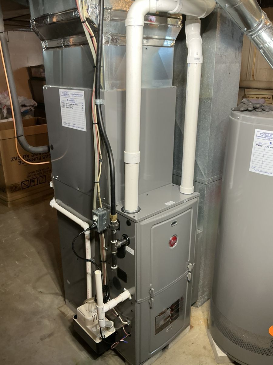 A grey, modern high-efficiency furnace with white PVC venting pipes in a basement, next to a water heater.