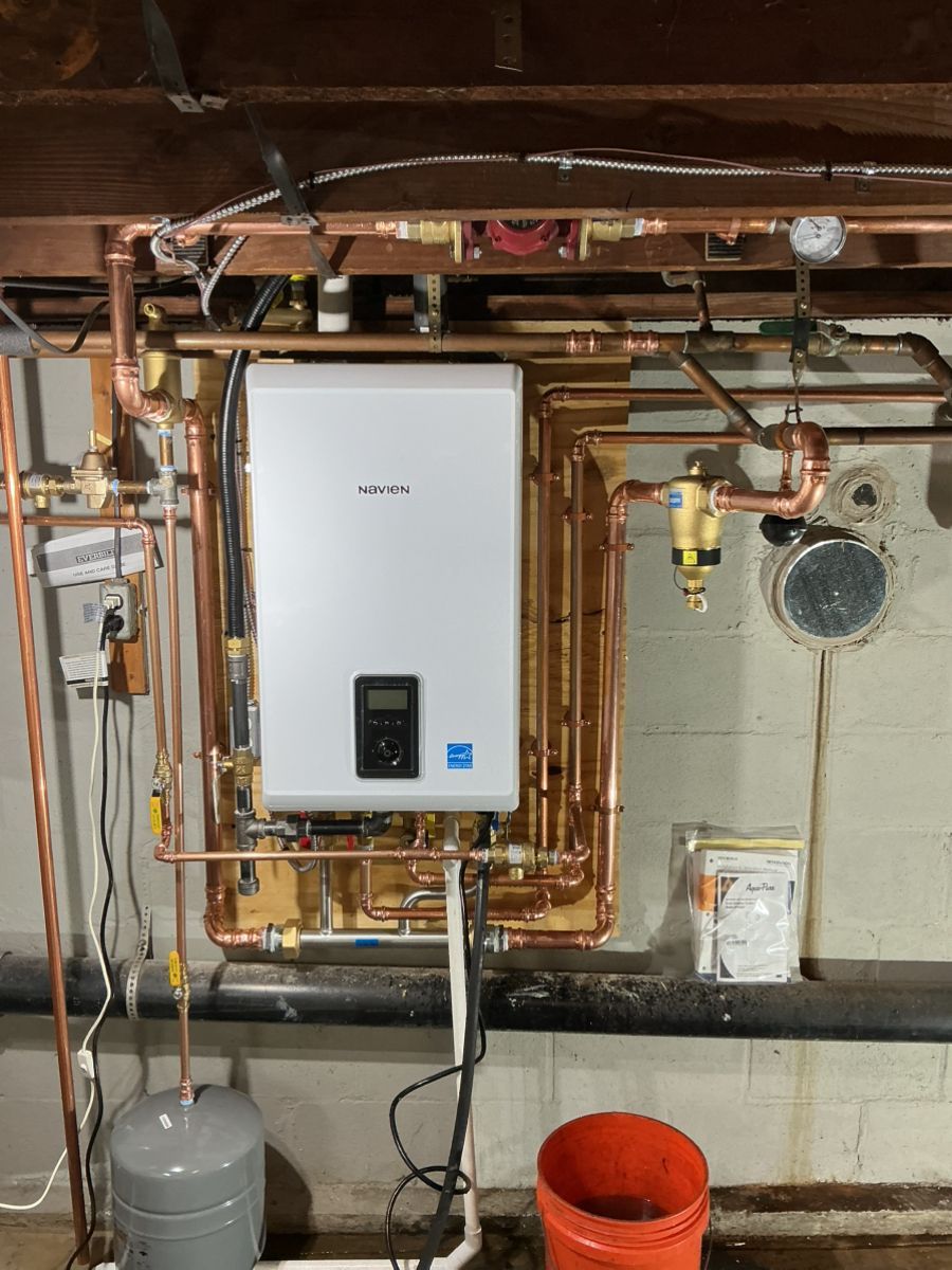Wall-mounted white tankless boiler unit installed against a basement wall with extensive copper plumbing connections.
