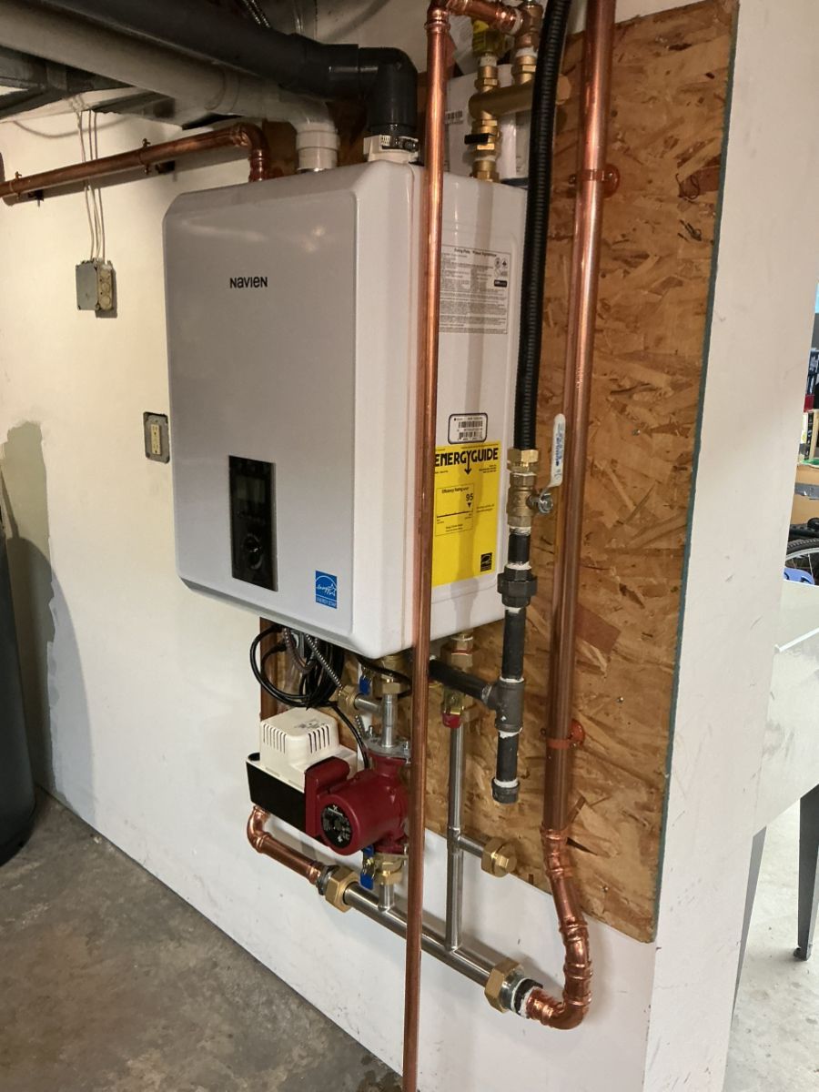 Wall-mounted Rinnai tankless water heater with copper plumbing, valves, and a red circulation pump on a plywood backboard.