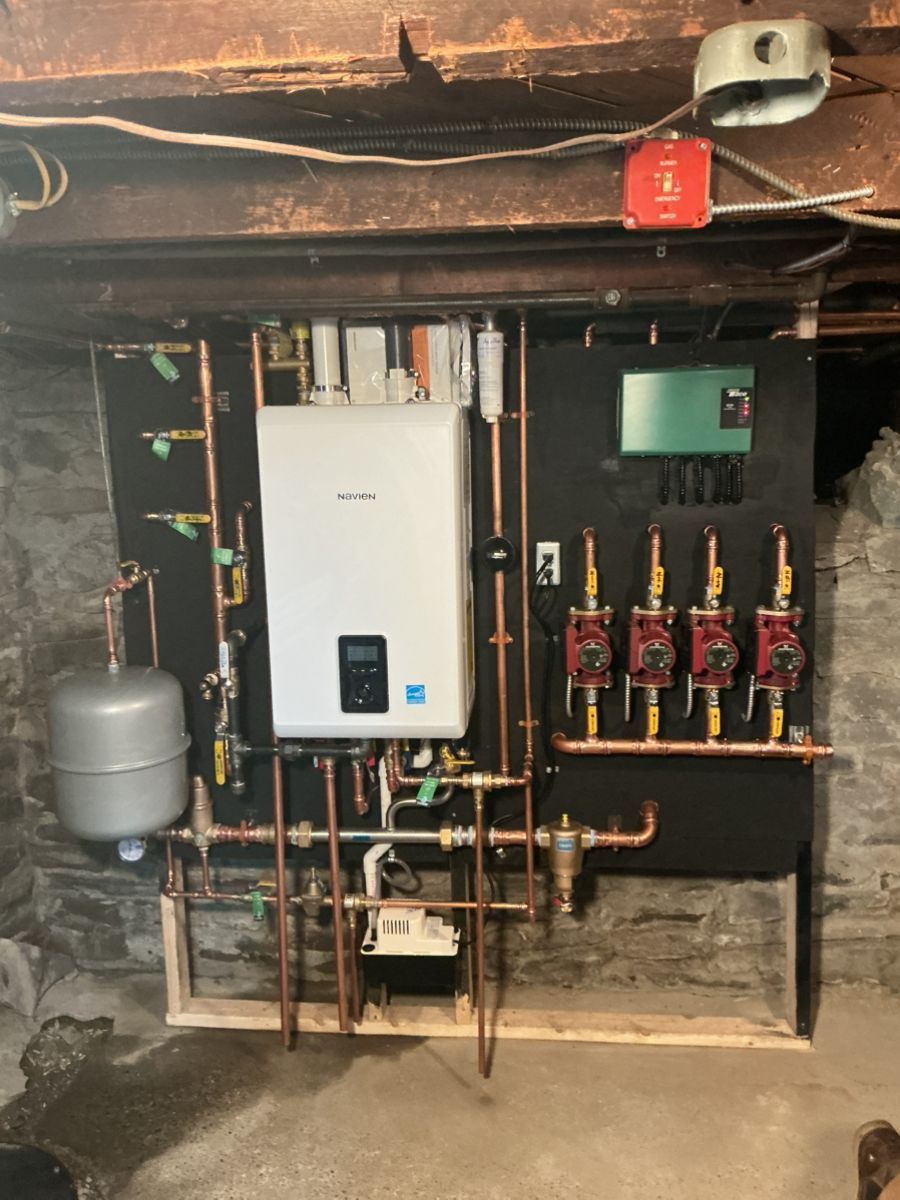Wall-mounted white boiler system with copper piping, circulator pumps, and an expansion tank in a basement.
