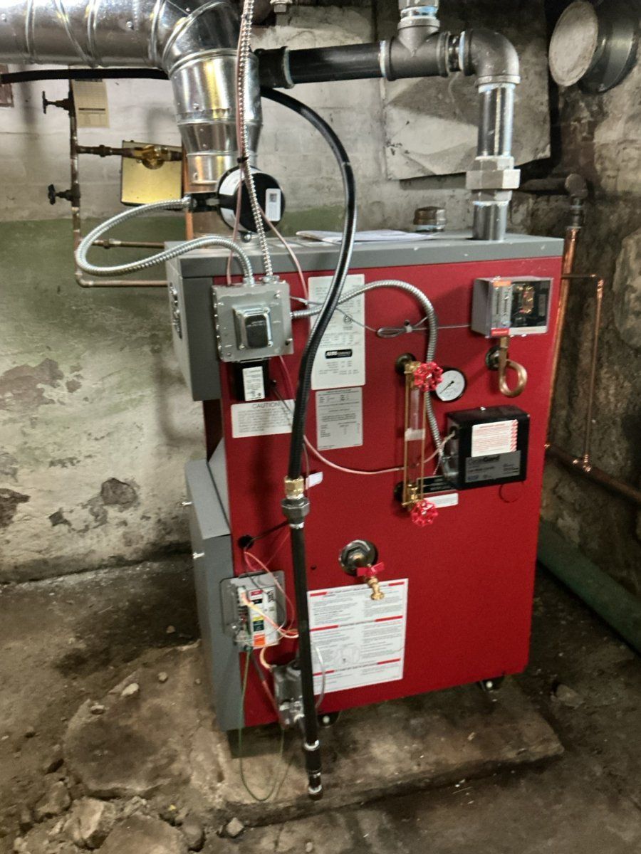 A red residential steam boiler with various pipes, valves, and electrical controls in a basement setting.