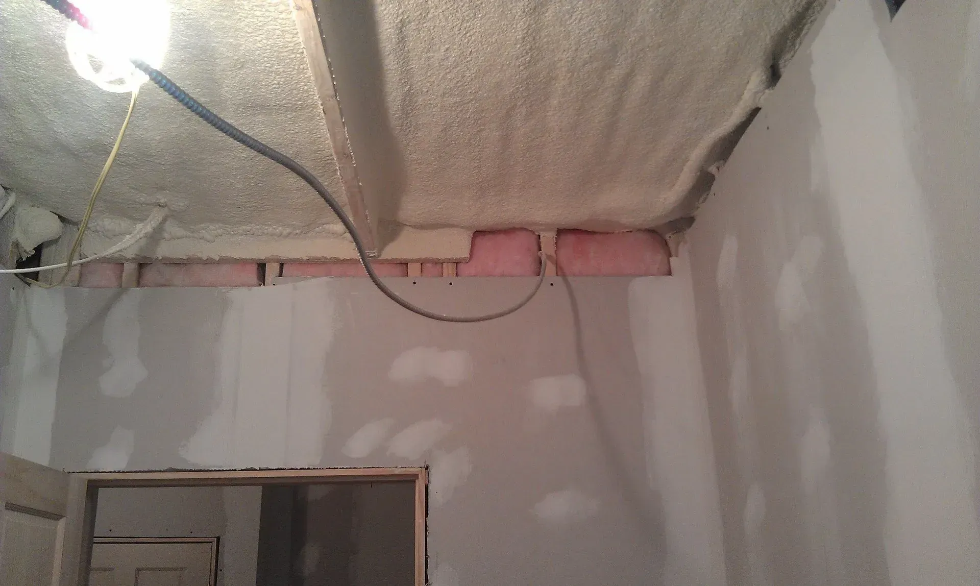 An unfinished room showing a textured ceiling with spray foam insulation, pink fiberglass wall insulation, and drywall.
