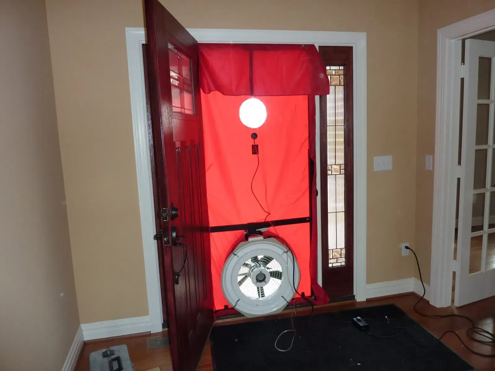 A blower door test setup with a red panel and fan installed in a residential front door frame to measure air leakage.