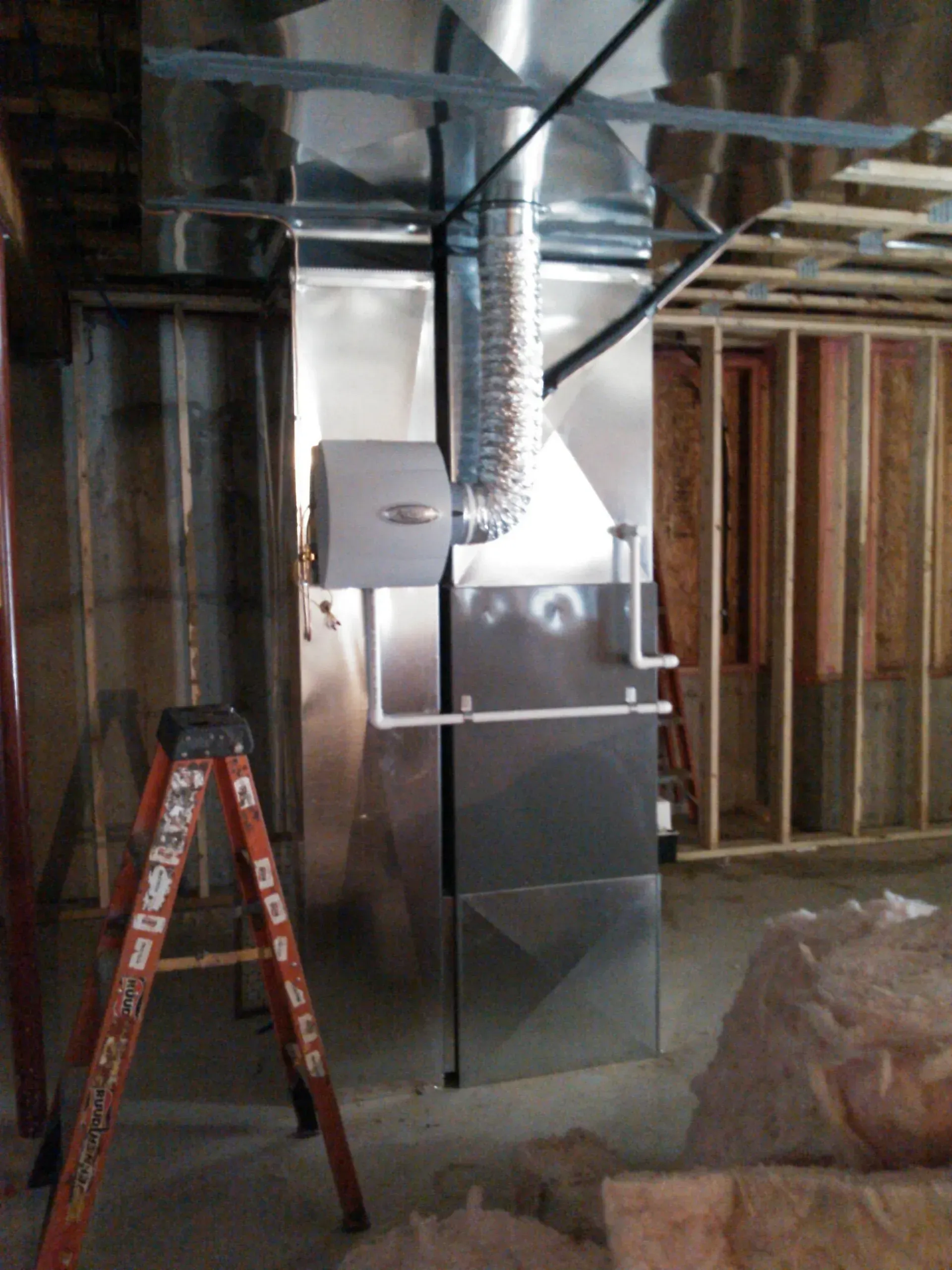 A furnace installed in an unfinished basement, featuring metallic ductwork, a humidifier, and white PVC piping.