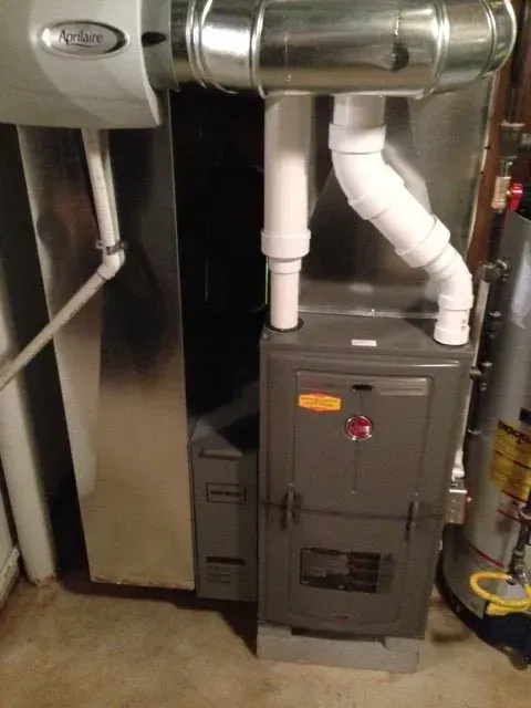 A modern high-efficiency HVAC furnace system with white PVC vent pipes and a mounted humidifier in a utility room.