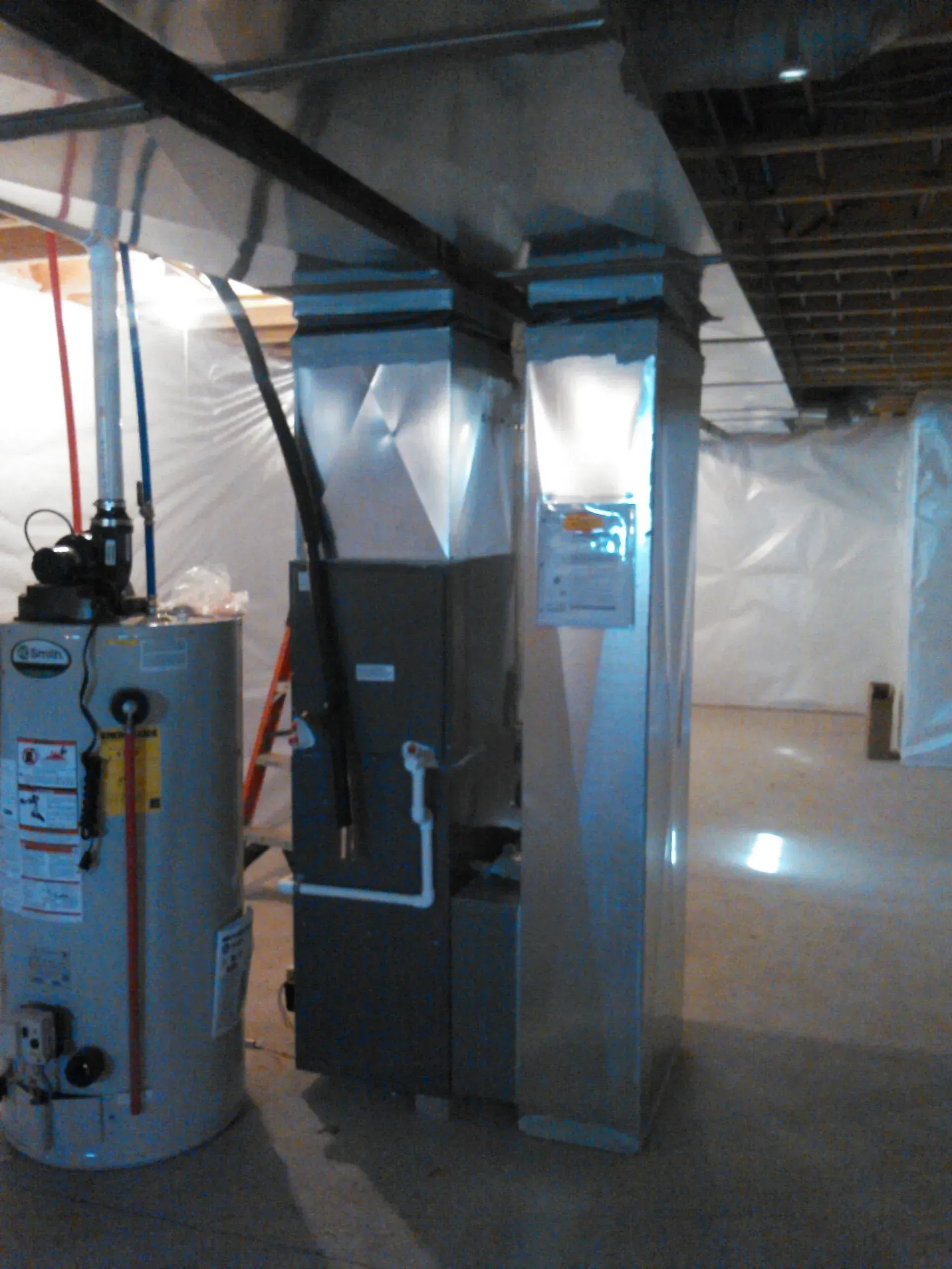 A basement utility area featuring a gray furnace and a metal water heater connected to silver overhead ductwork.