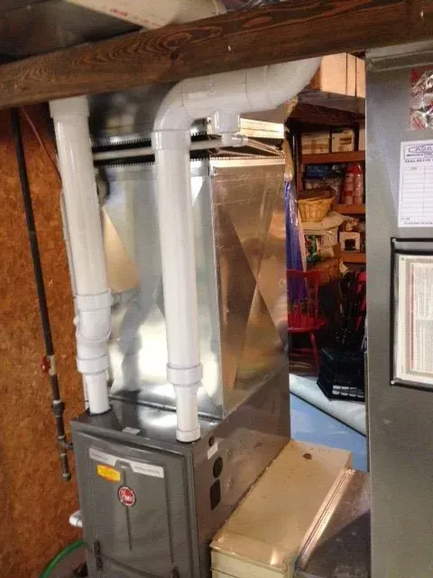 A high-efficiency gas furnace with white PVC intake and exhaust pipes installed in a basement utility area.