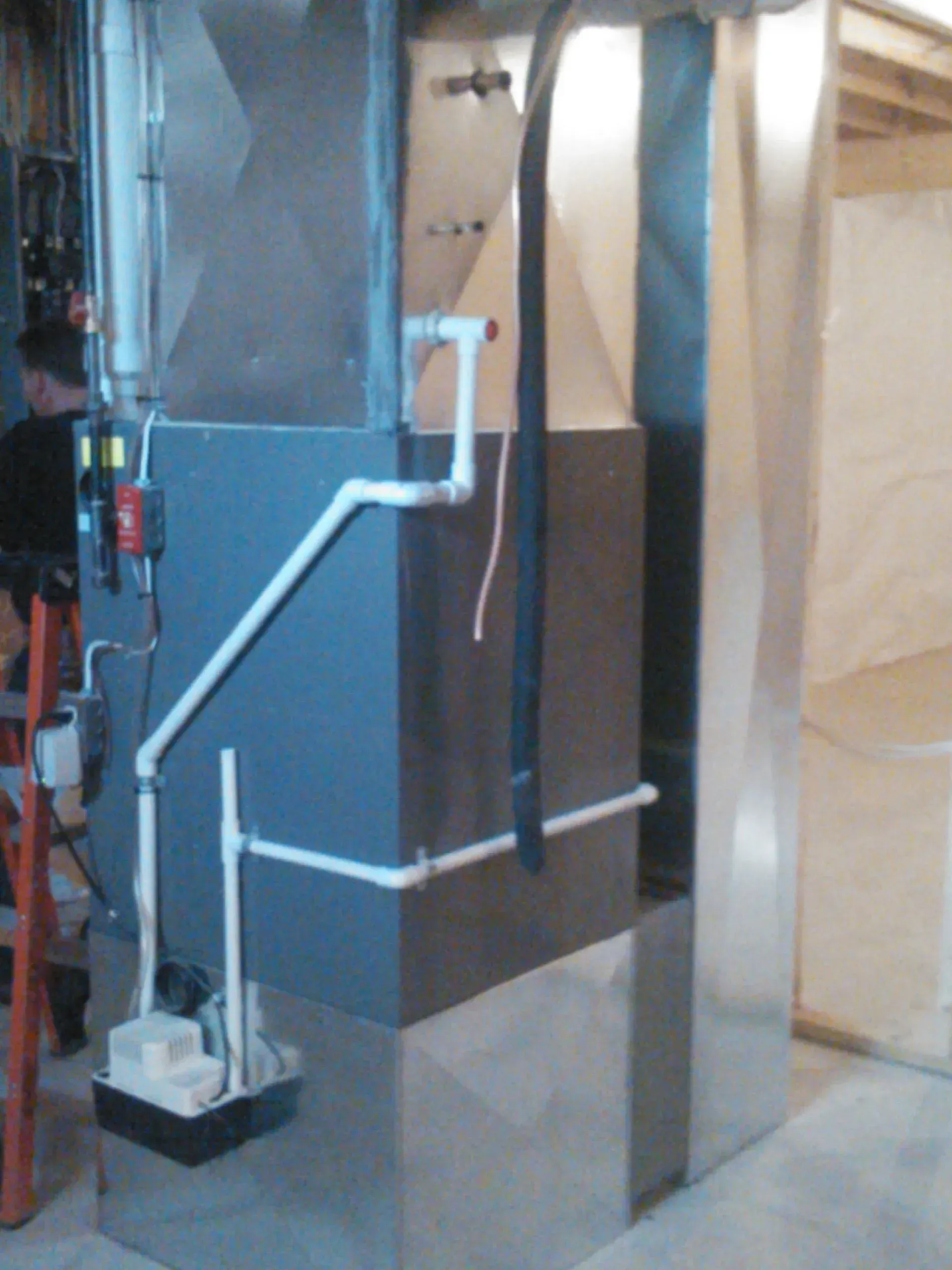A furnace unit in a basement with white PVC piping connected to a condensate pump on the side.