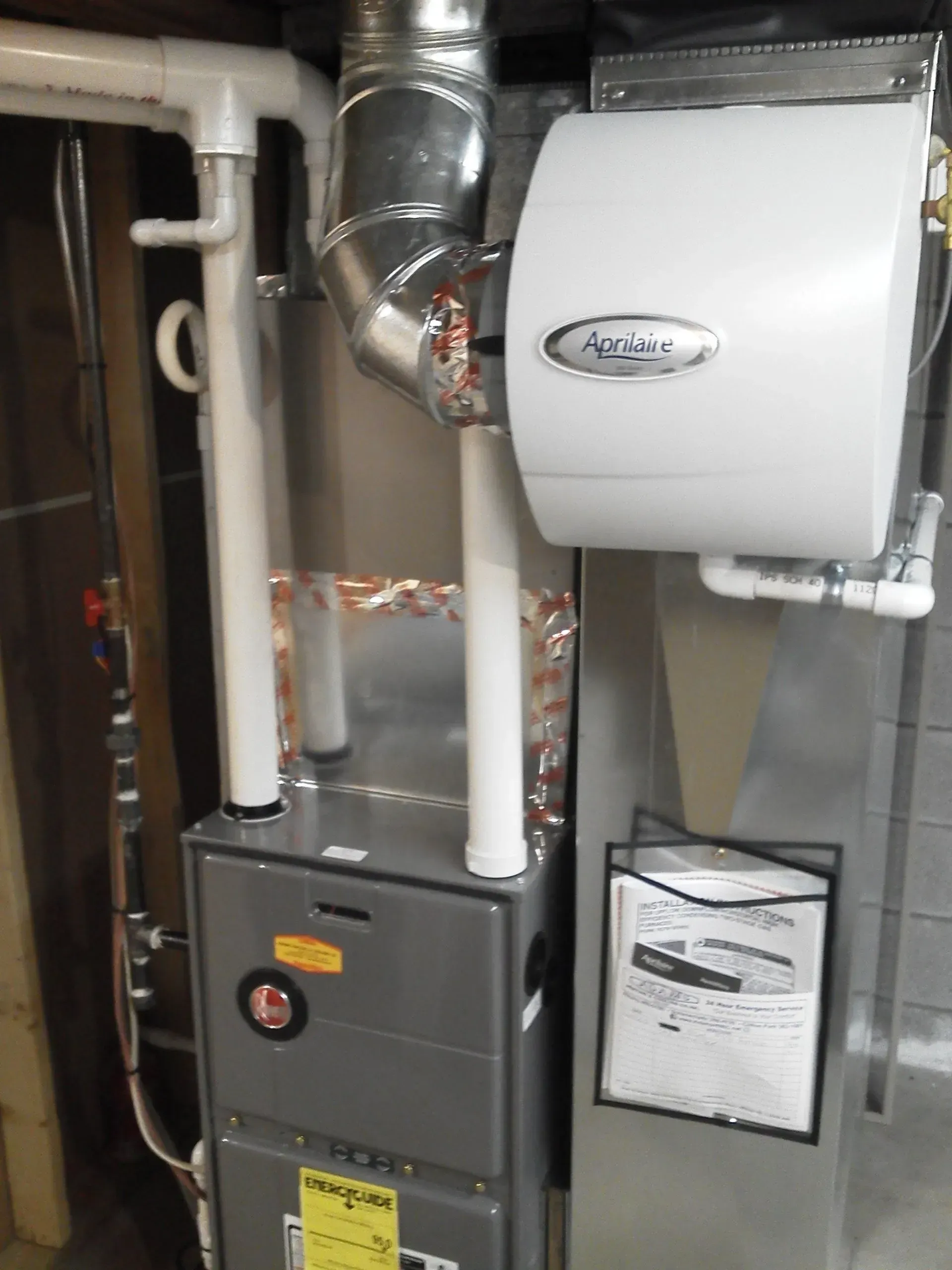A furnace and humidifier unit installed in a utility room with white PVC venting and silver metal ductwork.