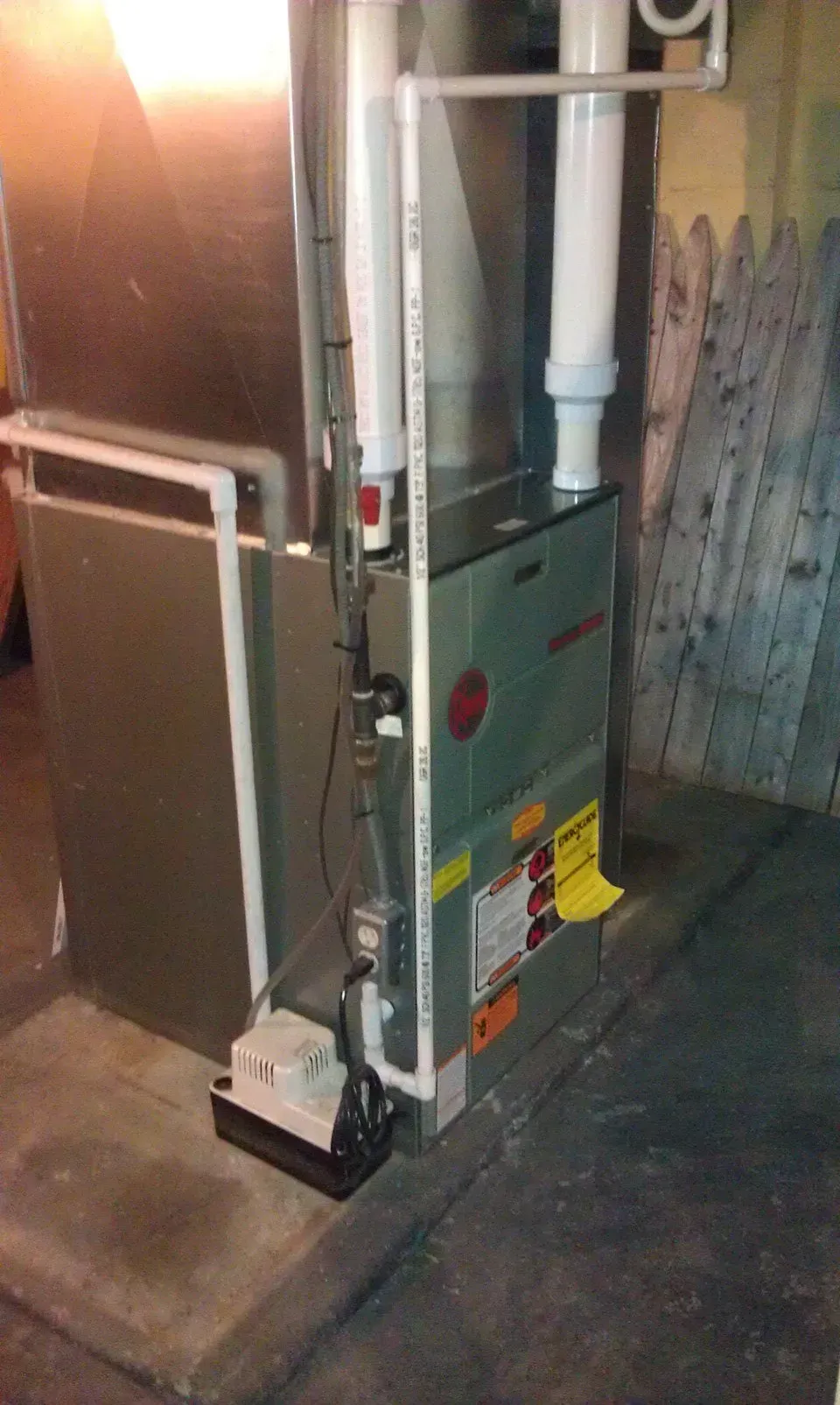 A grey high-efficiency gas furnace with white PVC venting pipes and a condensate pump on a concrete basement floor.