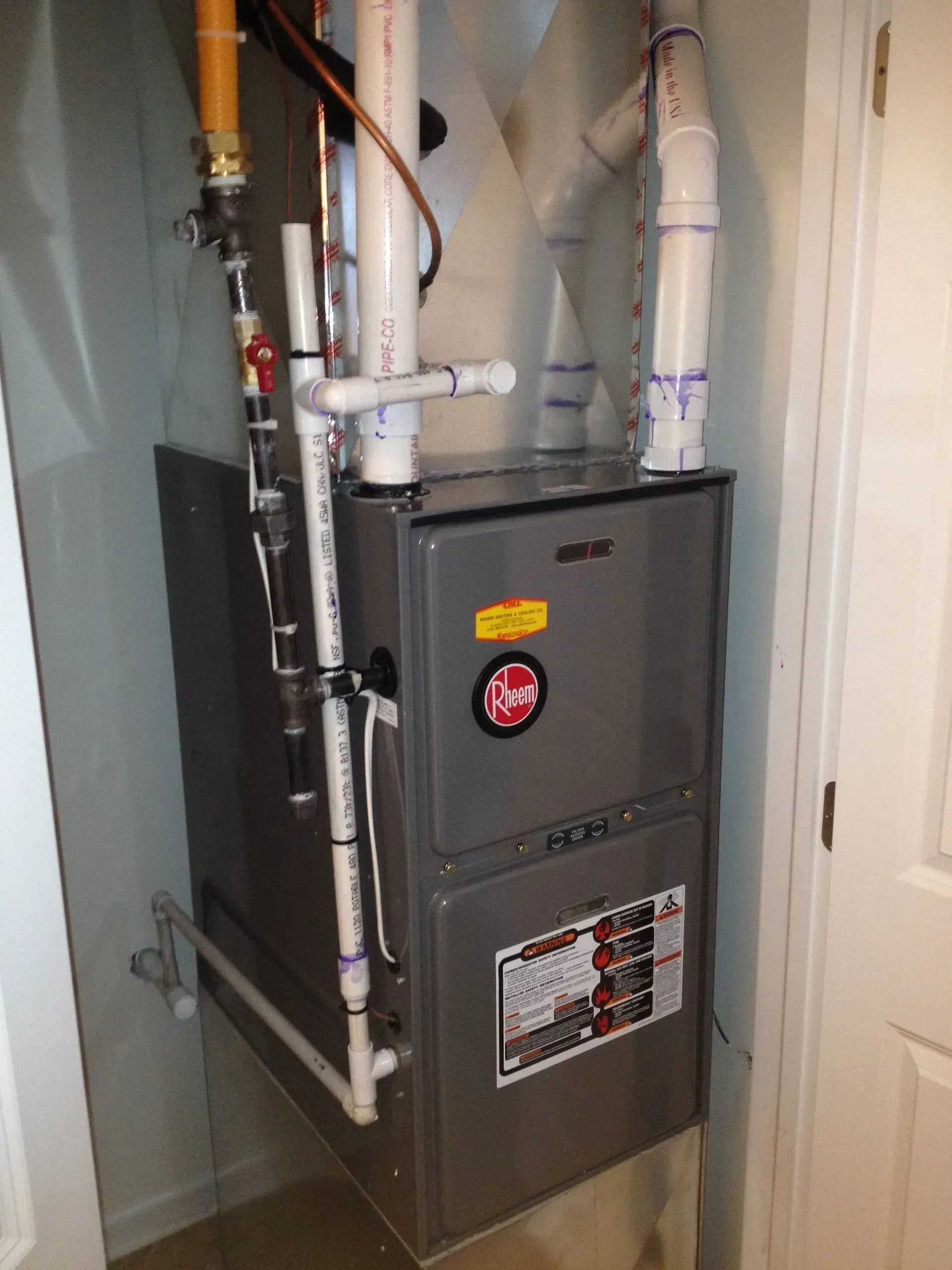A gray gas furnace with white PVC venting pipes installed in a utility closet.