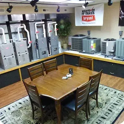 A conference table and chairs in a showroom displaying various HVAC heating and cooling units under Bryant signage.