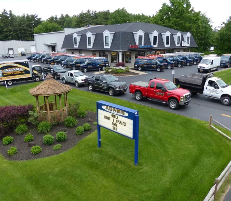 An elevated view of an Adams-branded commercial office building with a parking lot filled with company trucks and vans.