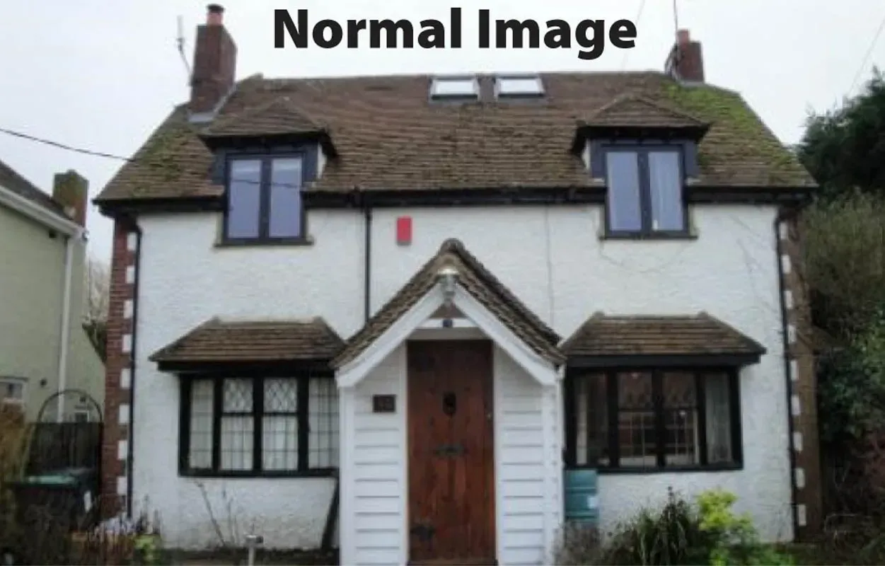 A two-story, white cottage with a pitched roof, dark-framed windows, and a central wooden front door with a peaked porch.
