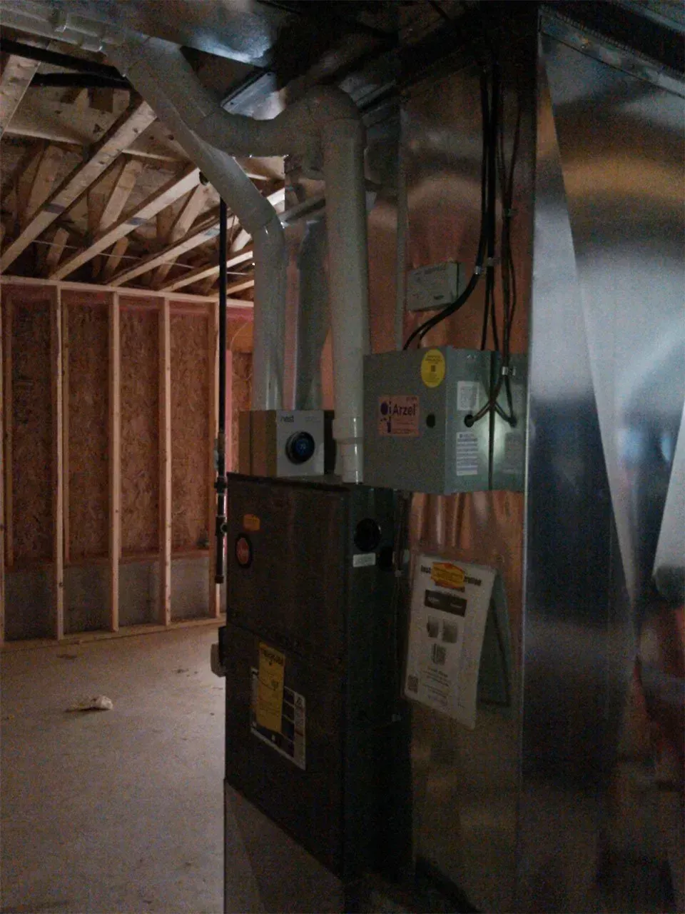 A high-efficiency gas furnace and silver ductwork installed in an unfinished basement with wooden wall studs.