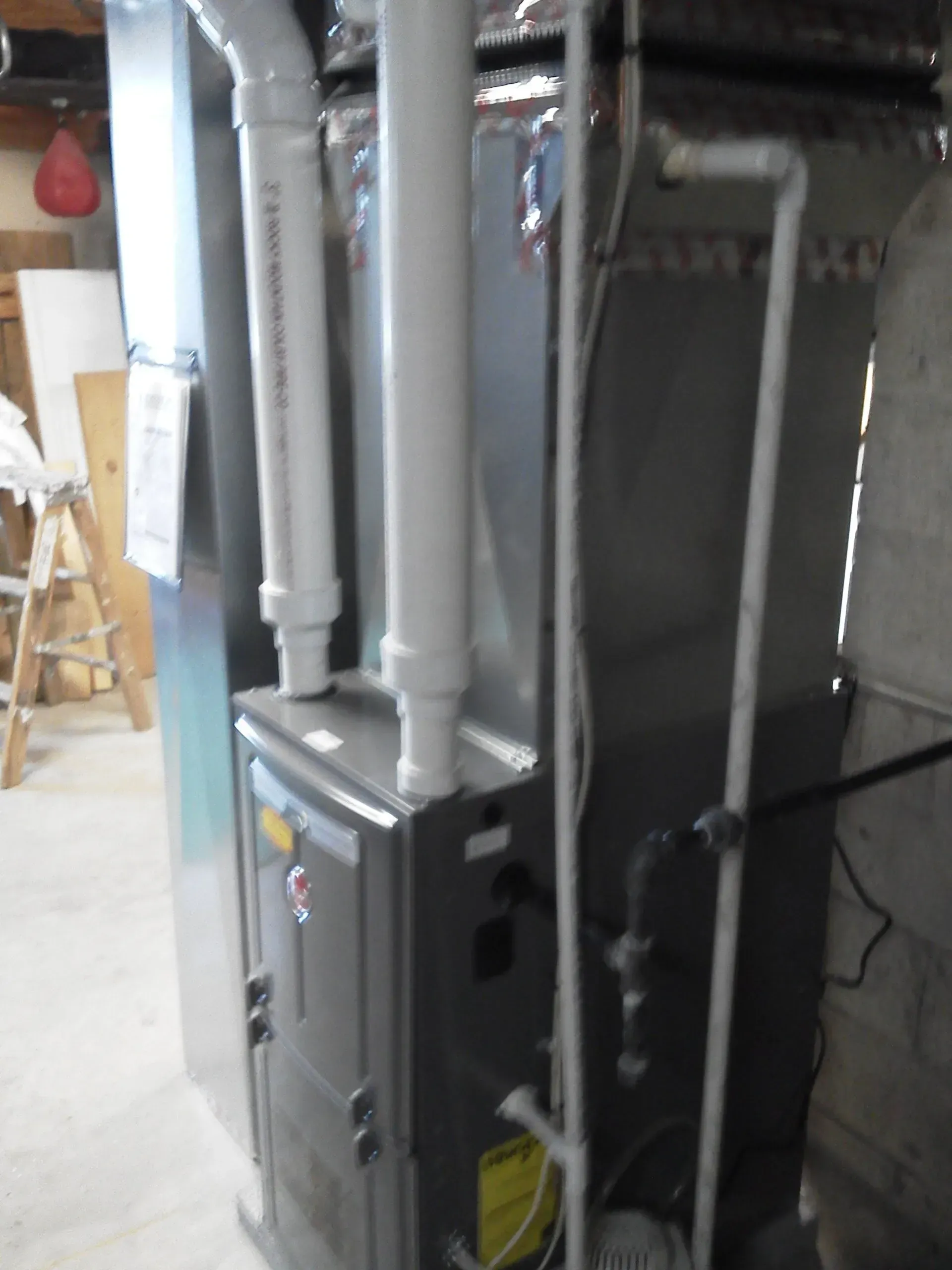 A gray high-efficiency furnace stands in a basement with connected white PVC venting pipes and a gas line.