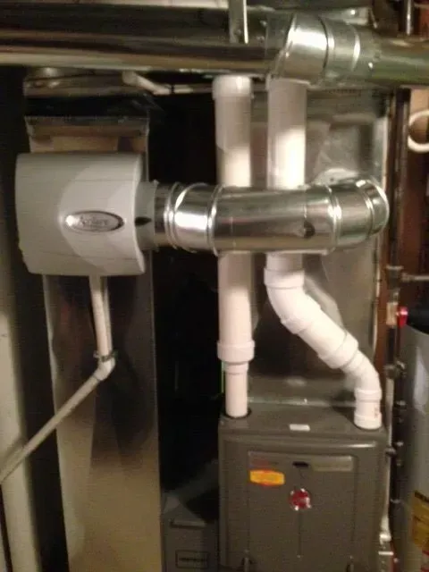 A high-efficiency furnace with white PVC exhaust pipes, metal venting, and a humidifier attached to the ductwork.