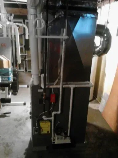 A dark grey gas furnace with white PVC piping, a red gas valve, and silver ductwork situated in a home basement.