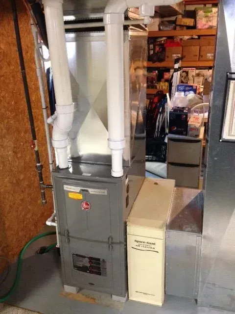 A high-efficiency furnace with vertical PVC venting pipes and an external air filter cabinet in a basement.