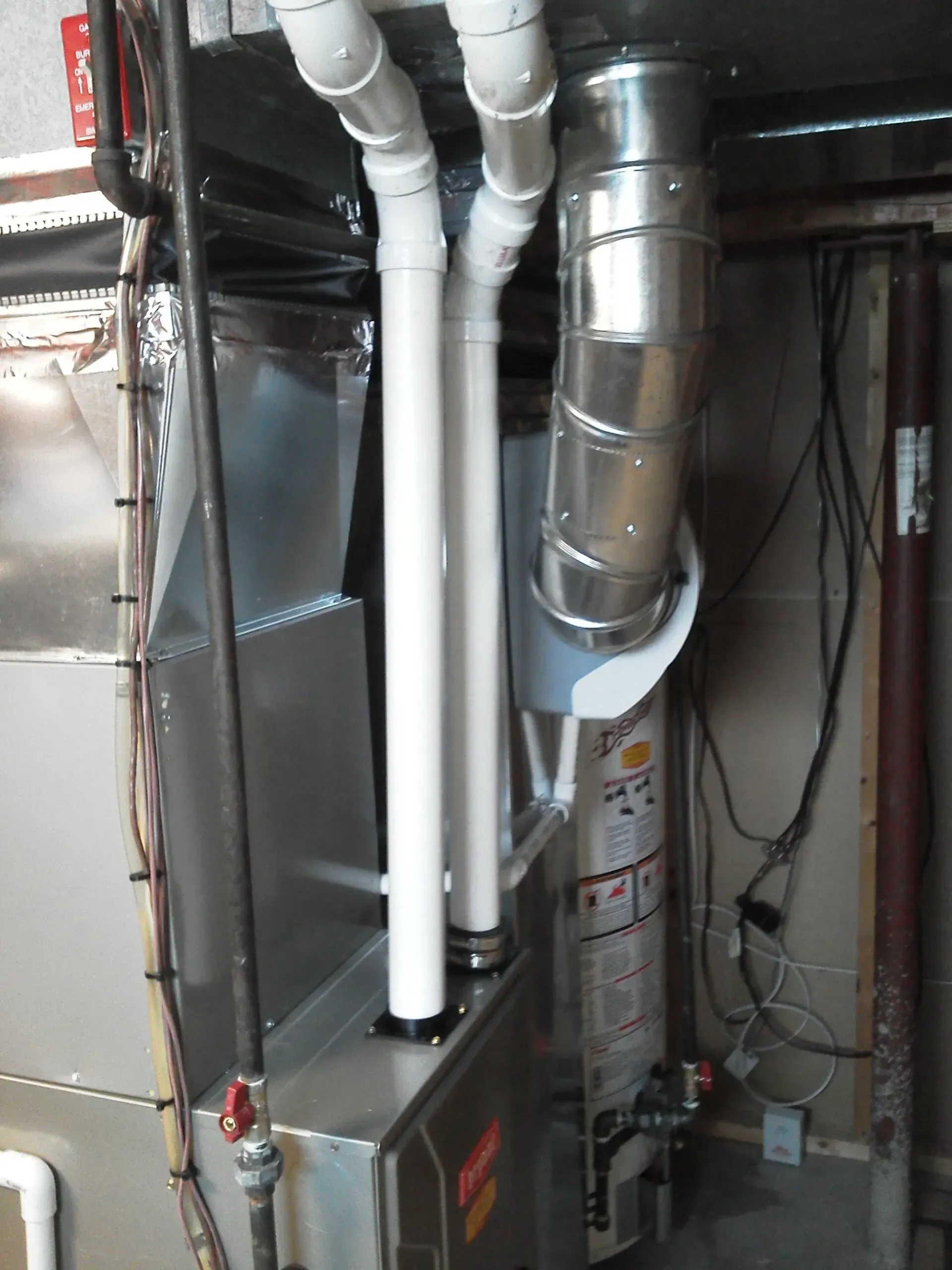 A furnace and water heater in a basement, showing white PVC intake and exhaust pipes and a silver metal flue.