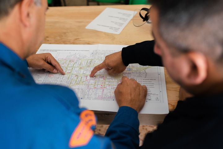 two men are sitting at a table looking at a map .