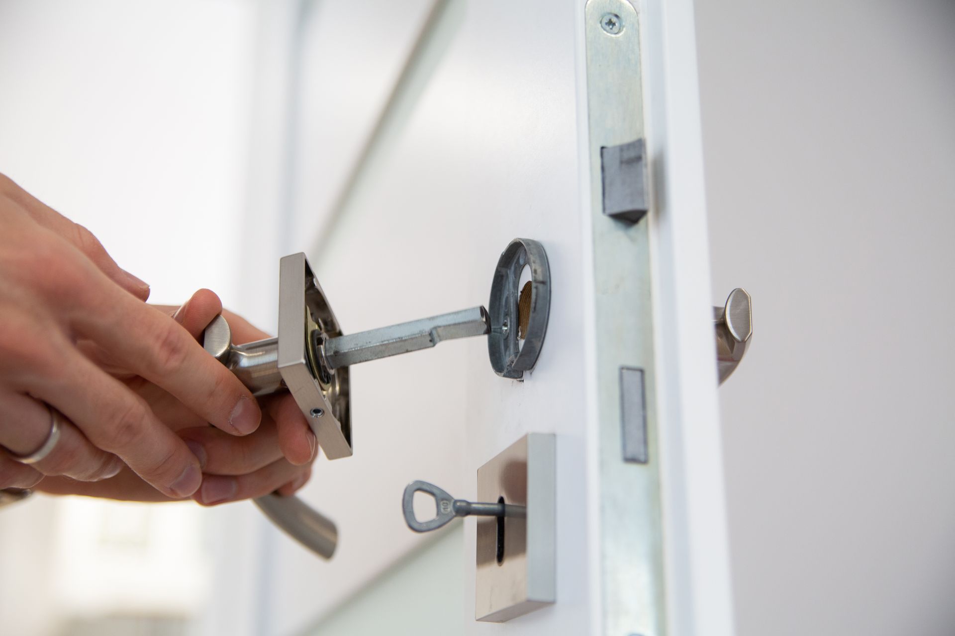 Hand turning a silver key in a white door lock, with a key dangling below