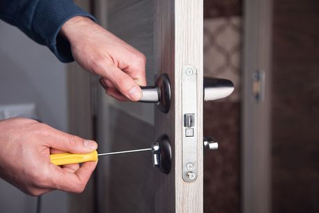 Hands using a screwdriver to remove a lock from a door latch.
