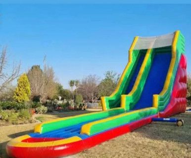 Inflatable double water slide, red, green, and blue, set on grass with trees and blue sky.