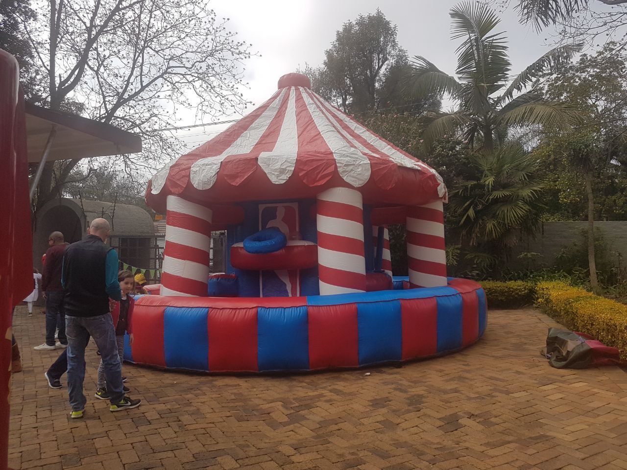 Inflatable circus-themed bounce house, red and blue, on paved area, with people in background.