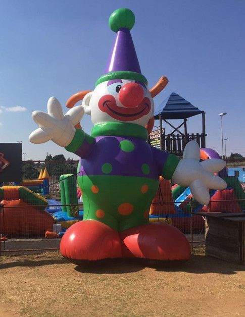 Giant inflatable clown, arms outstretched, on a sunny day in a playground setting.