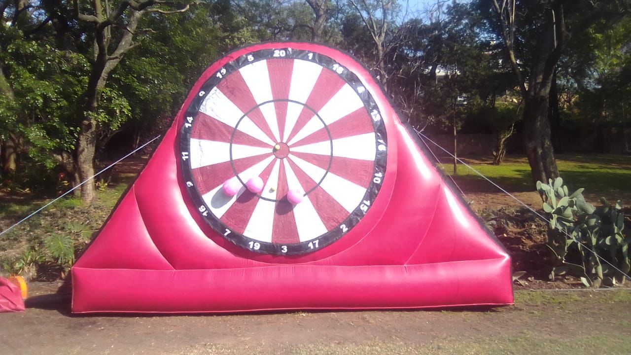 Inflatable red and white dartboard set up outdoors on grass. Two balls are stuck to it.