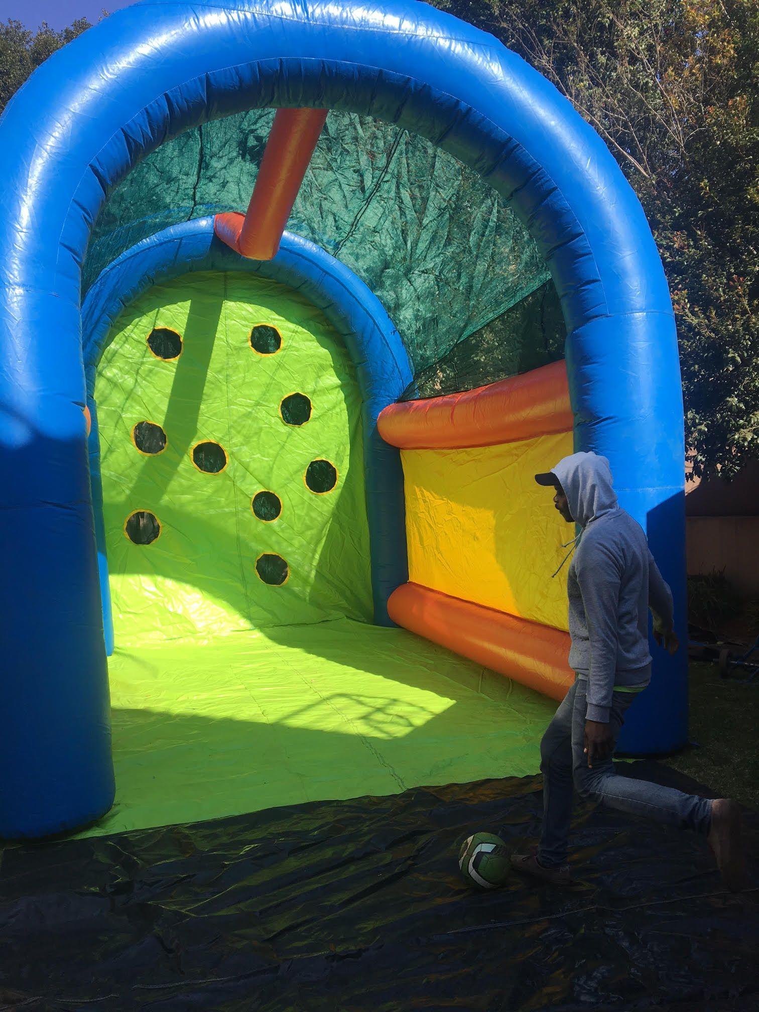 Person kicking a soccer ball towards an inflatable goal with holes.
